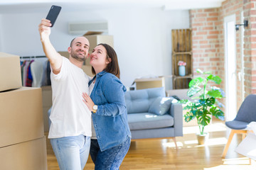 Fototapeta premium Young couple taking a picture photo using smartphone at new home, smiling happy for moving to new apartment