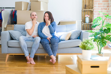 Fototapeta na wymiar Young couple sitting on the sofa arround cardboard boxes moving to a new house bored yawning tired covering mouth with hand. Restless and sleepiness.