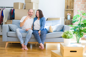 Fototapeta na wymiar Young couple sitting on the sofa arround cardboard boxes moving to a new house showing and pointing up with fingers number three while smiling confident and happy.