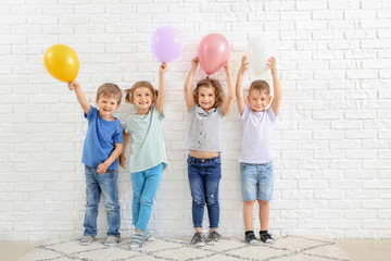 Cute little children with air balloons near white brick wall