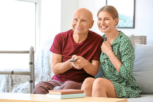 Young Woman And Her Elderly Father Watching TV In Nursing Home