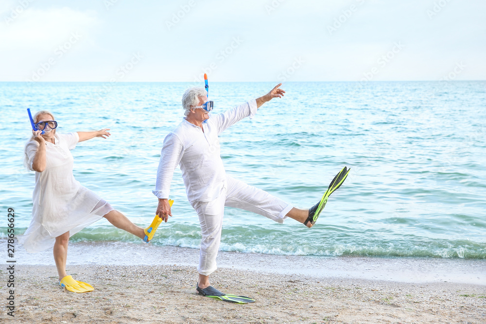 Wall mural happy mature couple with snorkeling masks and paddles having fun at sea resort