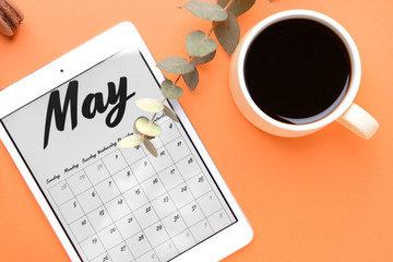 Tablet computer with calendar on screen and cup of coffee on color background