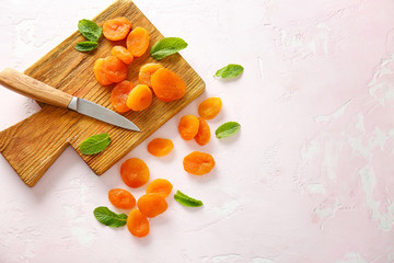 Board with dried apricots and knife on light background