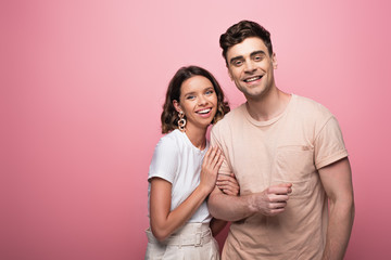 happy young woman hugging happy boyfriend on pink background