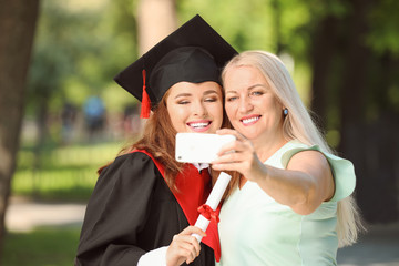 Happy young woman with her mother taking selfie on graduation day