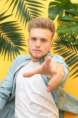 Stylish young man and tropical leaves on color background