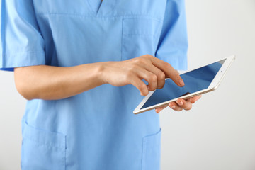 Nurse with tablet computer on light background, closeup