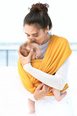 Young mother with her baby in sling walking outdoors