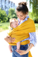 Young mother with her baby in sling walking in park