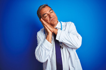 Handsome middle age doctor man wearing stethoscope over isolated blue background sleeping tired dreaming and posing with hands together while smiling with closed eyes.