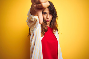 Young beautiful woman wearing red t-shirt and stripes shirt over yellow isolated background looking unhappy and angry showing rejection and negative with thumbs down gesture. Bad expression.