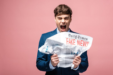 aggressive businessman crumpling newspaper with fake news while looking at camera