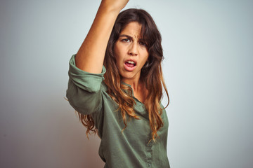 Young beautiful woman wearing green shirt standing over grey isolated background angry and mad raising fist frustrated and furious while shouting with anger. Rage and aggressive concept.