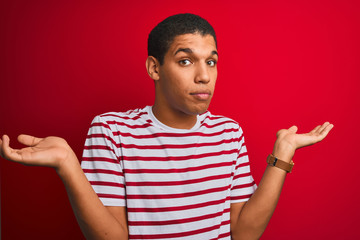 Young handsome arab man wearing striped t-shirt over isolated red background clueless and confused...
