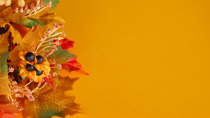 autumn colored leaves in a spray laying on an orange background with copy space