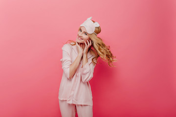 Glamorous curly girl expressing energy in morning. Pleasant caucasian woman in silk pyjama posing on pink background.