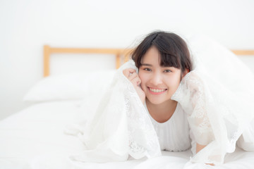 Beautiful portrait young asian woman lying and smile while wake up with sunrise at morning, girl with happy annd fun in the bedroom, lifestyle and relax concept.