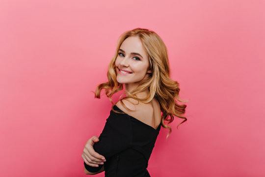 Enchanting glamorous girl looking over shoulder with shy smile. Studio shot of fashionable young caucasian woman in black clothes.