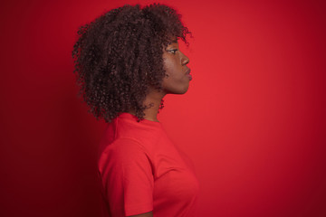 Fototapeta na wymiar Young african afro woman wearing t-shirt standing over isolated red background looking to side, relax profile pose with natural face with confident smile.
