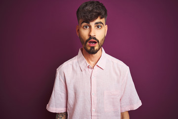 Young man with tattoo wearing summer pink shirt standing over isolated purple background afraid and shocked with surprise expression, fear and excited face.