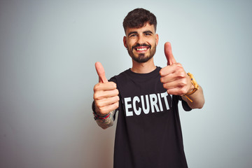 Young safeguard man with tattoo wering security uniform over isolated white background approving...
