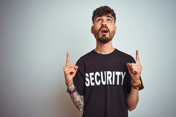 Young safeguard man with tattoo wering security uniform over isolated white background amazed and...