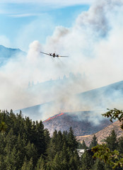 Airplane aircraft air tanker plane battling fighting wildland forest fire wildfire in Eastern Washington State. Smoke and flames engulf the landscape. Natural disasters.