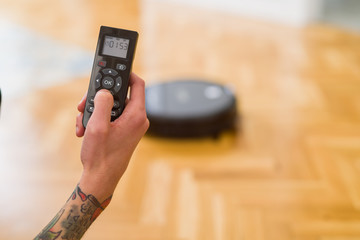 Close up of man hands controling automatic vacuum cleaner using electronic control of the mopping...