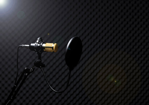 Microphone Condenser, gold mic with filter hang over sound absorbing wall room in dark audio studio, low exposure shadow silhouette studio lighting background copy space
