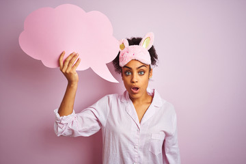 Afro woman wearing pajama and mask holding speech bubble over isolated pink background scared in shock with a surprise face, afraid and excited with fear expression