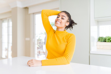 Beautiful african american woman with afro hair wearing a casual yellow sweater smiling confident touching hair with hand up gesture, posing attractive and fashionable