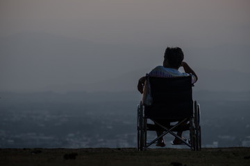 Silhouette The elderly sit on the wheelchair at the view point at sunset time.