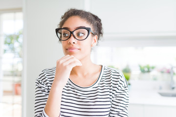 Beautiful young african american woman with afro hair wearing glasses with hand on chin thinking about question, pensive expression. Smiling with thoughtful face. Doubt concept.