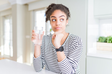 Young african american girl drinking a fresh glass of water serious face thinking about question, very confused idea