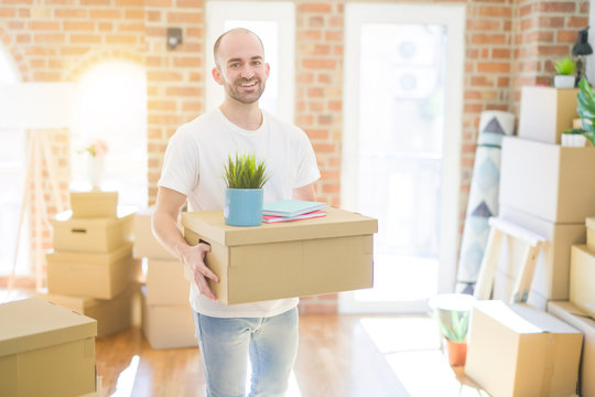 Young handsome man moving to a new house, holding cardboxes smiling very happy for new apartment