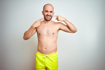 Fototapeta premium Young shirtless man on vacation wearing yellow swimwear over isolated background smiling cheerful showing and pointing with fingers teeth and mouth. Dental health concept.