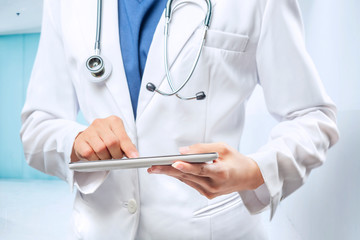 Woman doctor in white lab coat and stethoscope using tablet