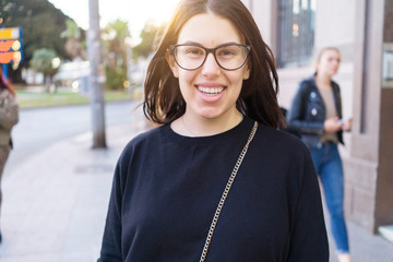 Beautiful young brunette woman smiling excited walking down the city streets, happy and confident expression standing outdoors at the town