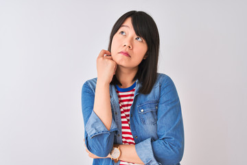 Chinese woman wearing denim shirt and red striped t-shirt over isolated white background with hand on chin thinking about question, pensive expression. Smiling with thoughtful face. Doubt concept.