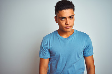 Young brazilian man wearing blue t-shirt standing over isolated white background Relaxed with serious expression on face. Simple and natural looking at the camera.