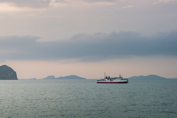 Huge boat or ferry with dark smoke float on the ocean at sunset time