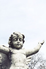 Sculpture of angel in the cemetery park. Stone statue of angel praying.