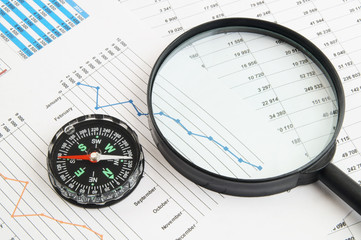Navigation in financial world concept, magnifying glass and compass on financial charts and graphs