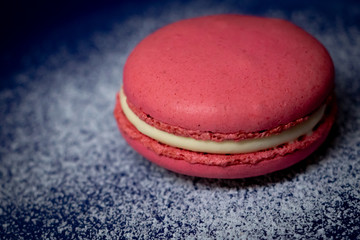 Pink Macaron or Macaroon in blue dish on wooden table. A colorful small and sweet French pastry of made of almond flour and egg whites.
