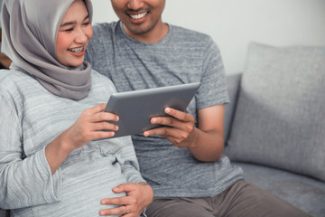 muslim pregnant woman using tablet pc with husband in livingroom