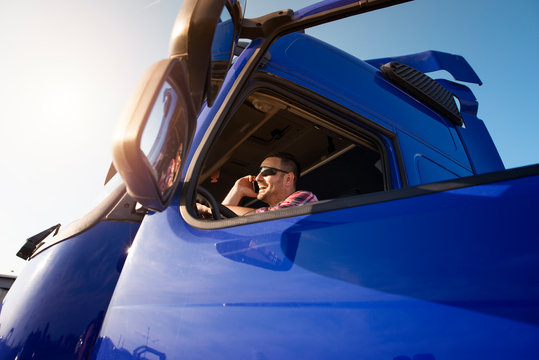 Truck Driver Sitting In The Cabin Of Freighter Talking On The Phone Checking His Route. Transportation Service.