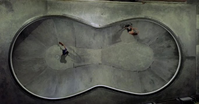 Cinematic aerial drone footage of two hipster millennials skateboarding in concrete pool at night. Modern active lifestyle. Extreme sport on summer vacation. Bird eye top view. Bali Indonesia.