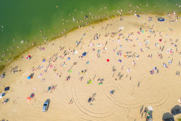 Aerial shot of people sunbathing and swimming on sunny day on beach near pond. Top view of coast with vacationers and fun people.