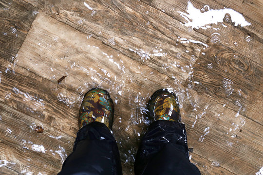 Woman's Feet Wearing Waterproof Boots, Standing In A Flooded House With Vinyl Wood Floors.